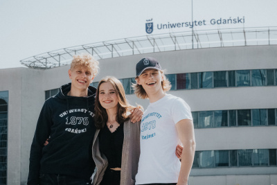 troje studentów na tle wejścia na wydział, nad budynkiem napis Uniwersytet Gdański