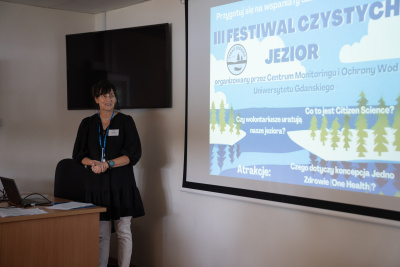 Prof. Julita Dunalska w sali wykładowej, w tle monitor z wyświetlonym plakatem III Festiwalu Czystych Jezior