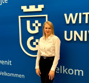 Dr Halyna Alekseievska na tle granatowej ściany z białym logo Uniwersytetu Gdańskiego