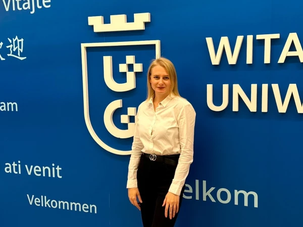 Dr Halyna Alekseievska na tle granatowej ściany z białym logo Uniwersytetu Gdańskiego