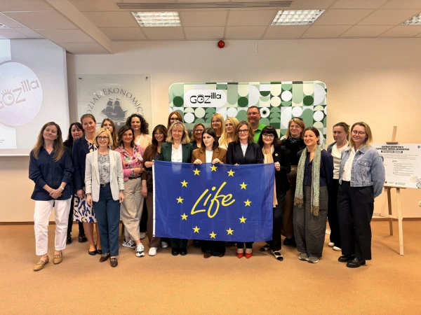 Zdjęcie grupowe uczestników seminarium; stoją na tle planszy z nazwą projektu, przed sobą trzymają flagę opartą na fladze UE z napisem LIFE w środku okręgu z gwiazd