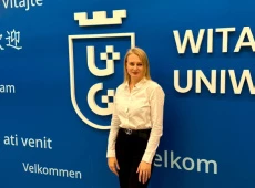 Dr Halyna Alekseievska na tle granatowej ściany z białym logo Uniwersytetu Gdańskiego
